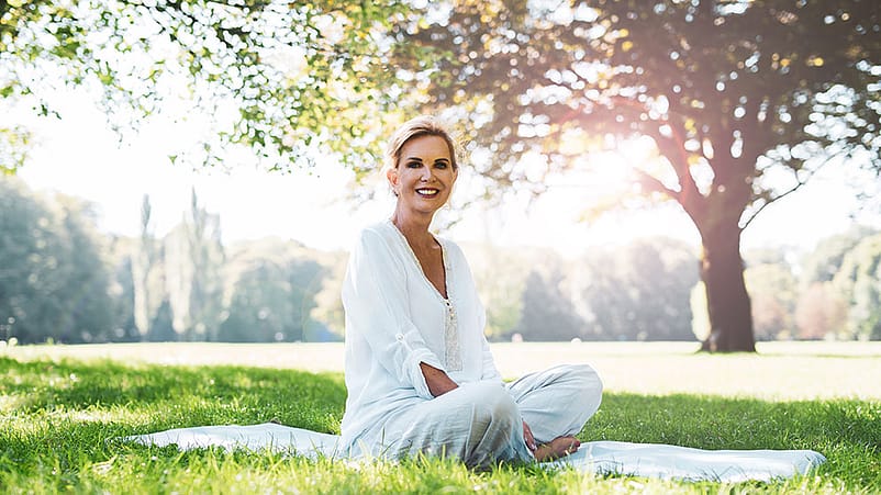 Eine aeltere Frau sitzt im Park auf einer Decke