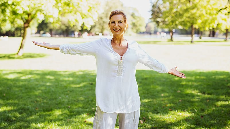 Une femme âgée et heureuse étend les bras dans le parc.