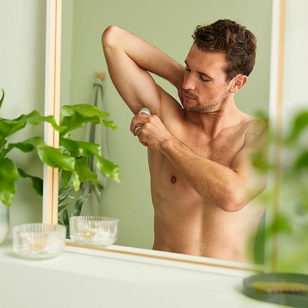 Mann im Badezimmer traegt Deo auf