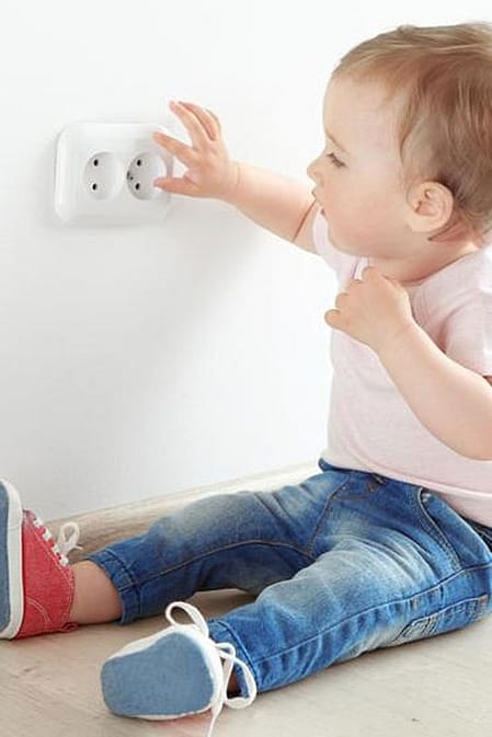 Niño pequeño sentado en el suelo jugando con el enchufe de una casa