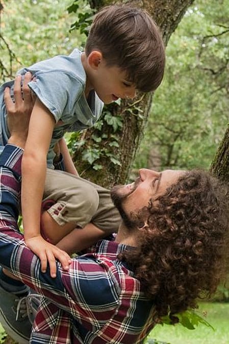 Man holding a child above his arms in a forest.