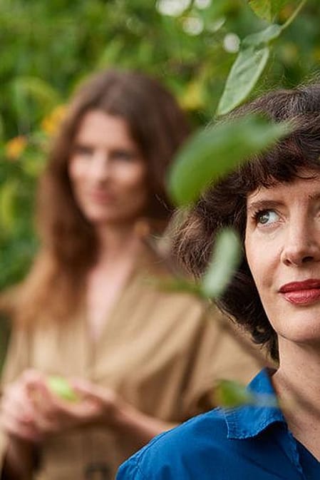 Women standing behind tree leaves.
