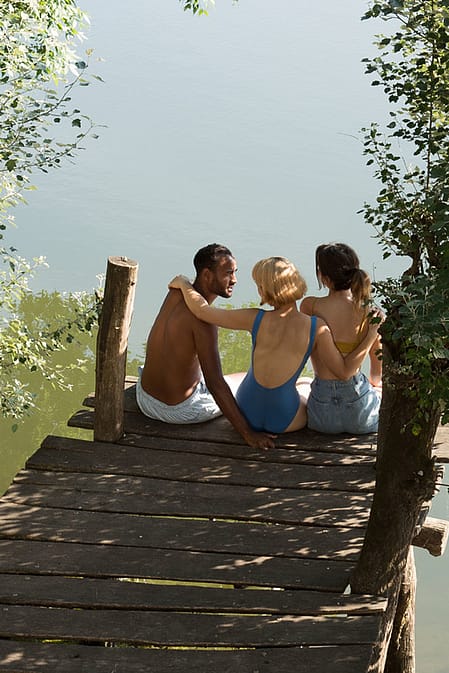 Three friends are sitting on a jetty by the lake.