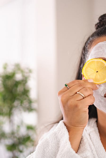 žena s pleťovou maskou drží před obličejem plátek citronu