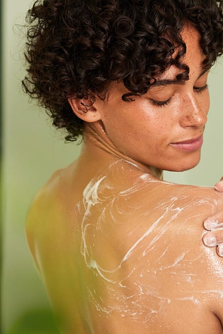 žena provádí peeling těla ve sprše