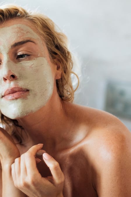 Žena v koupelně aplikuje čistící pleťovou masku
