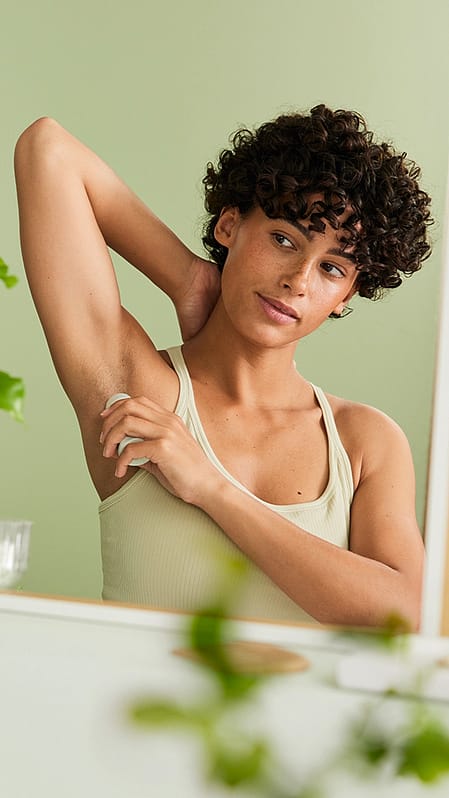 Woman applying deodorant infront of the mirror.