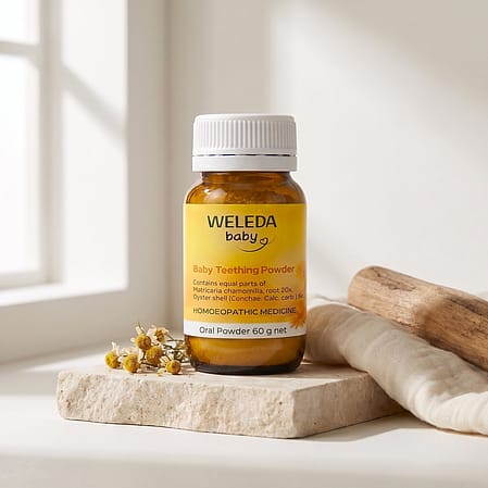 Weleda Baby Teething Powder jar with chamomile flowers next to it.