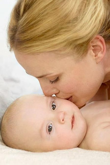 mujer dando un beso a un bebé tumbado sobre una cama