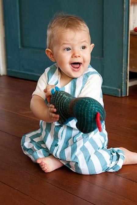 Bebé sonriendo y sentado en el suelo con un juguete en las manos