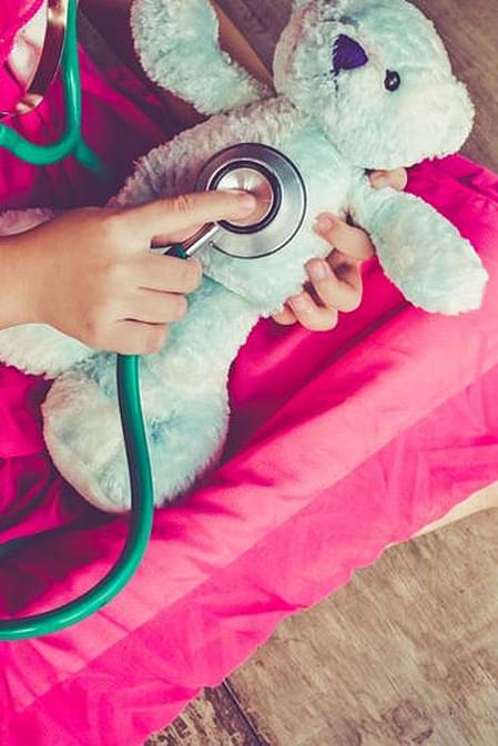 niña sentada en el suelo auscultando a su peluche con un fonendo