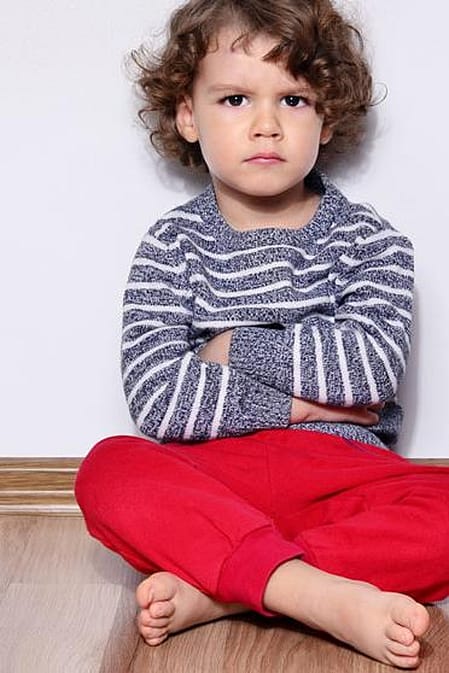 niño enfadado con los brazos cruzados sentado en el suelo