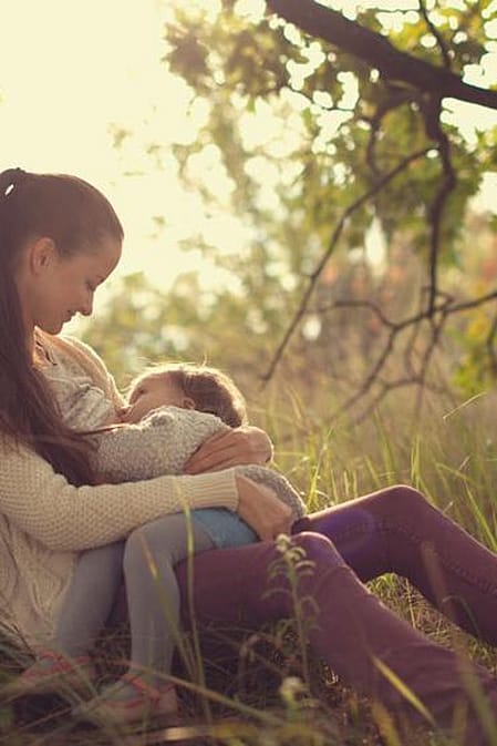 Une femme allaite, assise sous un arbre