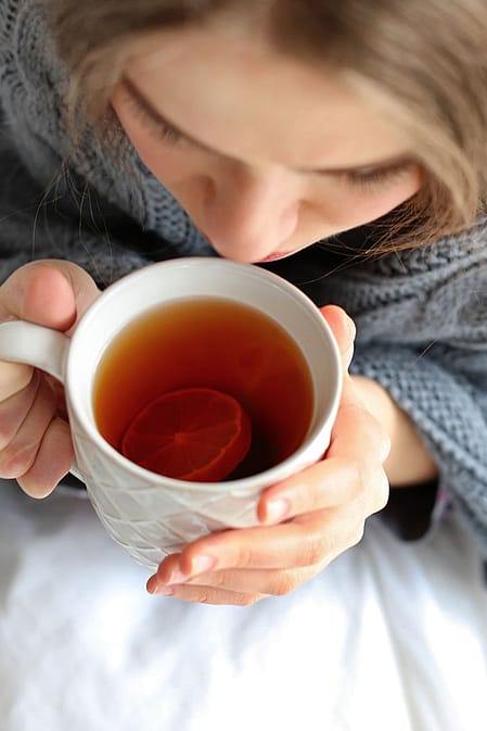 Frau ist eingehuellt in einen dicken Schal und trinkt Tee