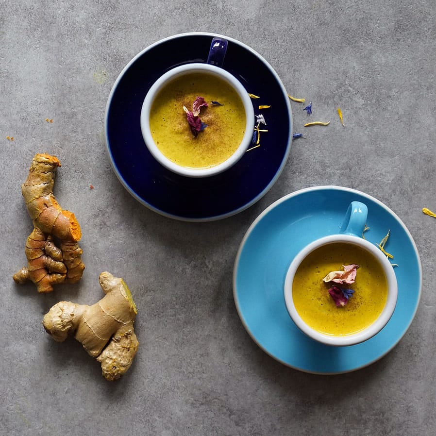 zwei blaue Tassen mit veganer Moonmilk neben einer gelben Kurkumawurzel