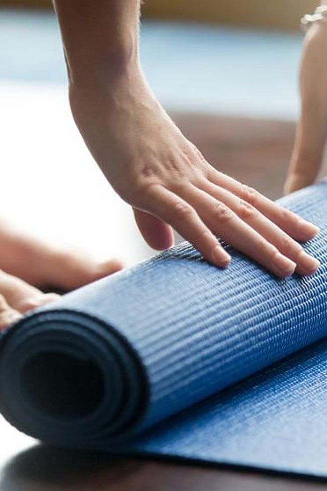 Eine Frau rollt einen Yogateppich zusammen