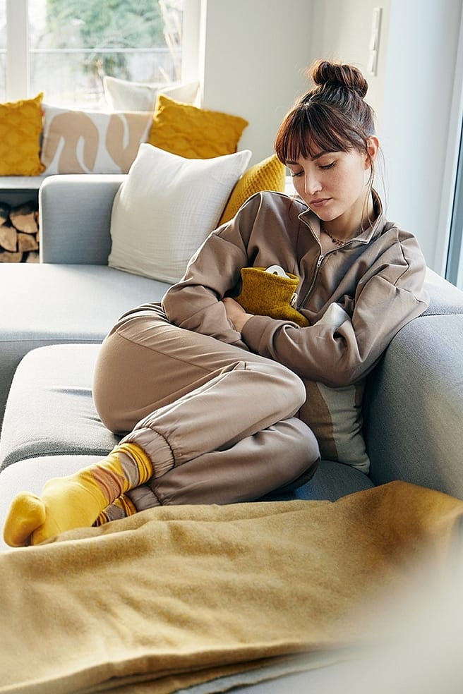 Frau mit Waermflasche auf dem Bauch auf einem Sofa