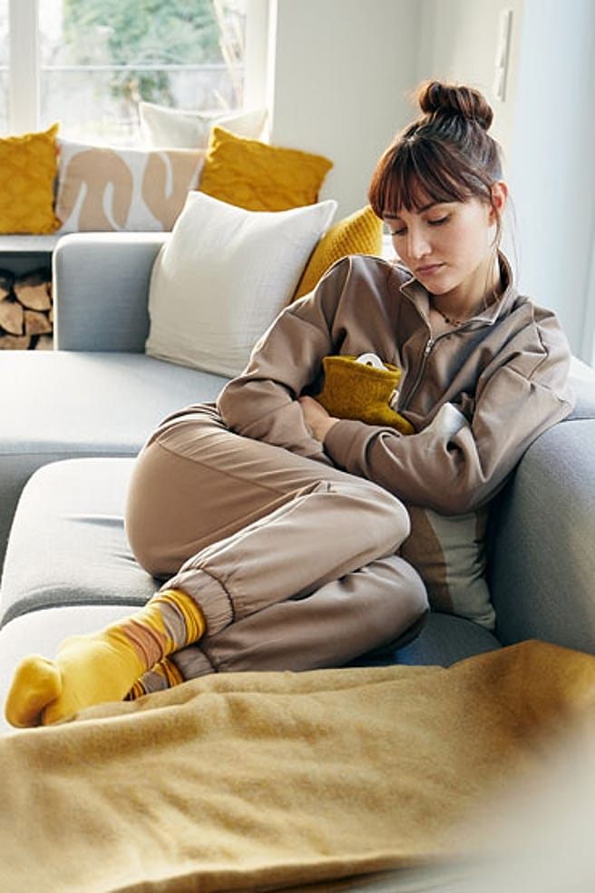 Frau mit Wärmeflasche auf dem Sofa im Wohnzimmer