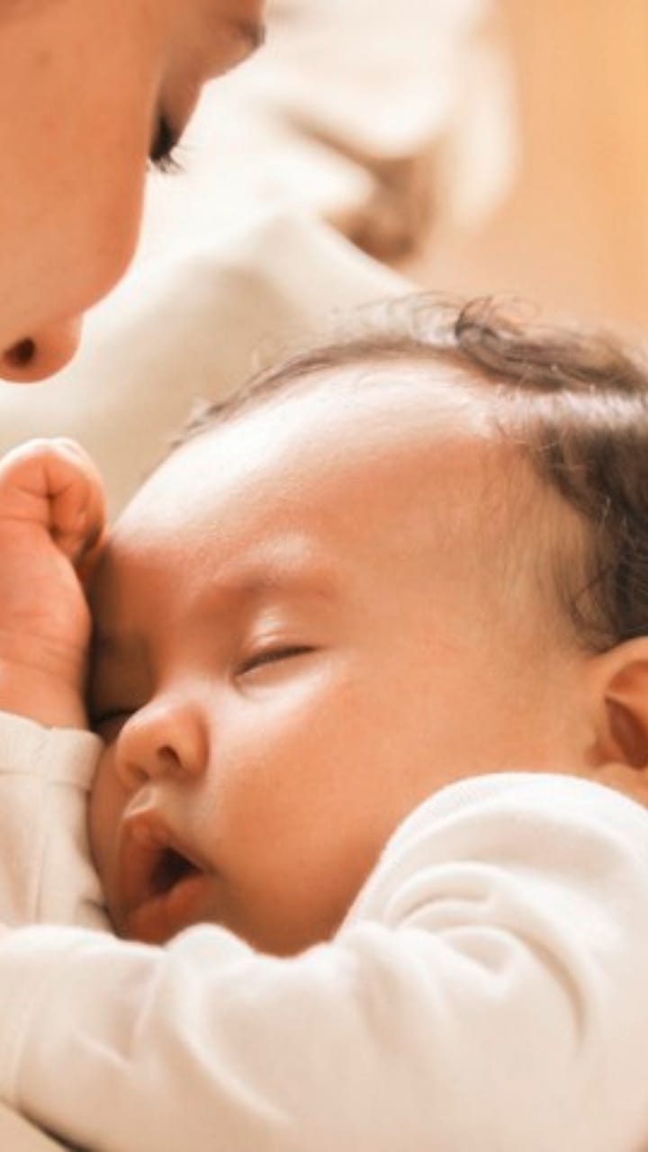 bebé dormido en los brazos de una mujer que lo mira dormir