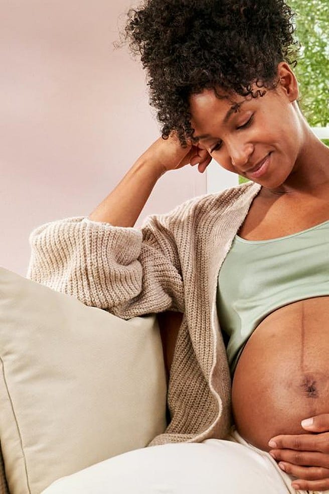 Gravid kvinna sitter i soffan men handen på magen.