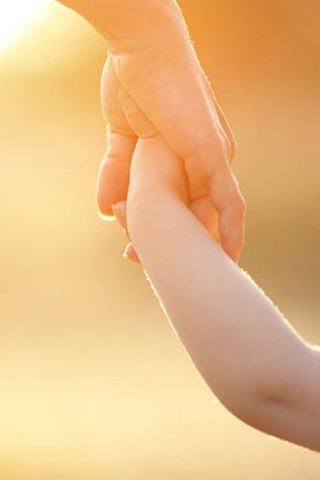 niño dándole la mano a una mujer con el atardecer de fondo