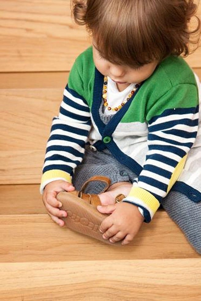 niño poniendose los zapatos sentado en una escalera con un juguete al lado