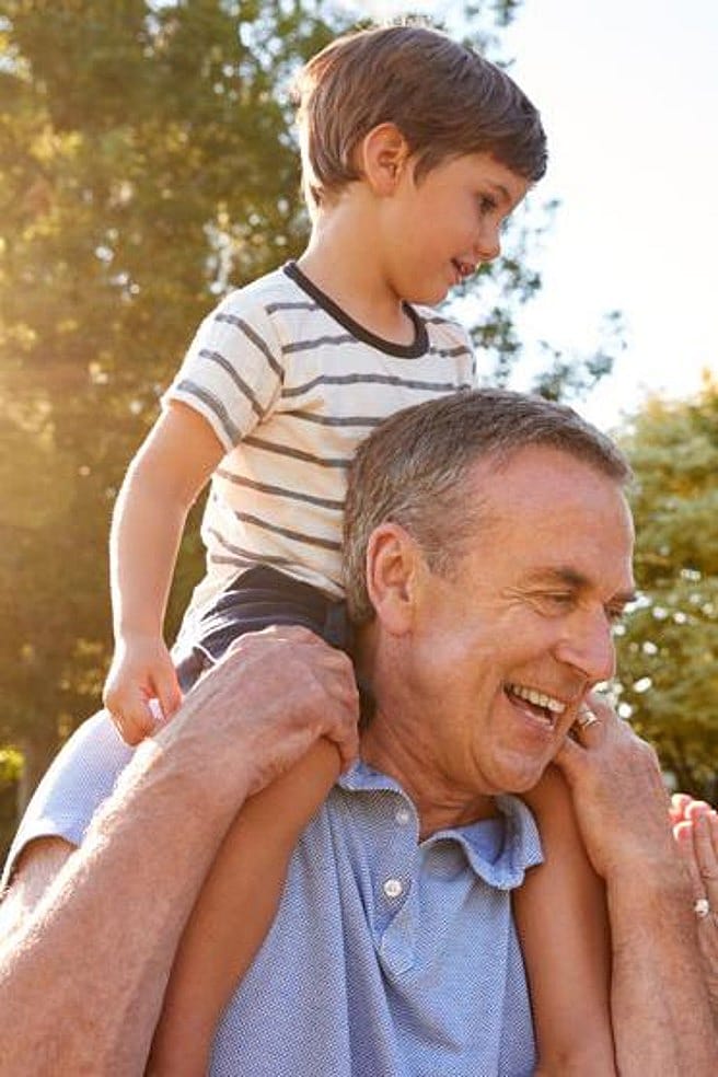niño sentado en los hombros de su abuelo mientras su abuela les mira