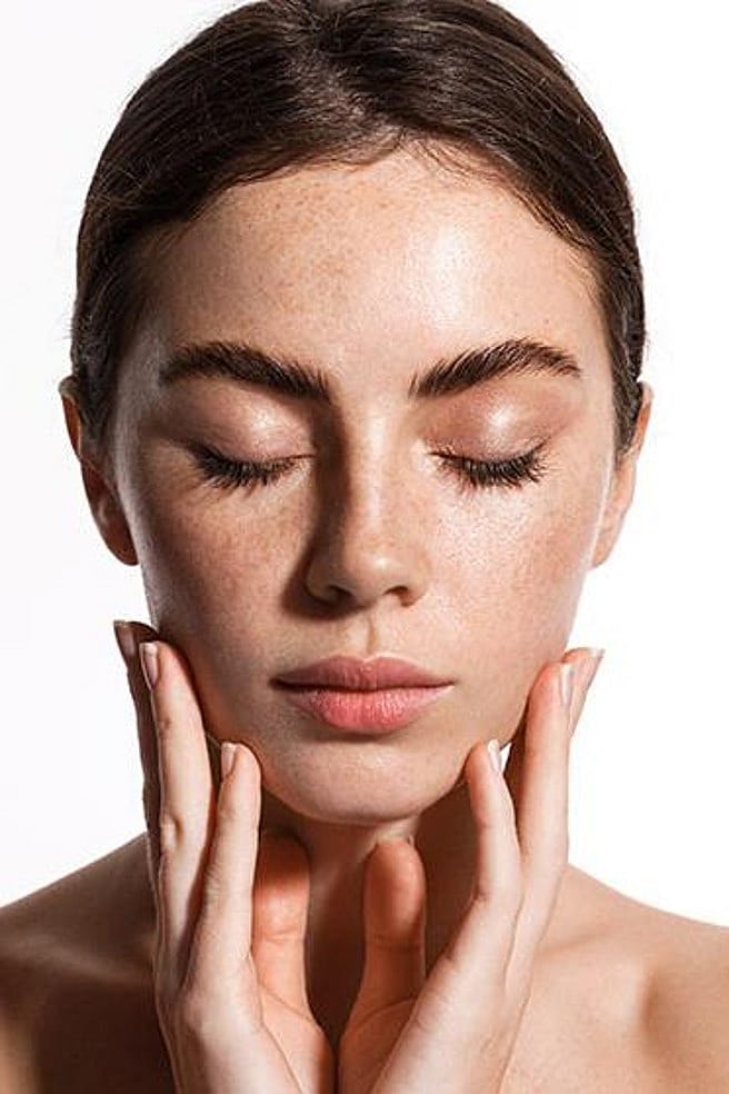 Entspannte junge Frau haelt ihr Gesicht in den Haenden