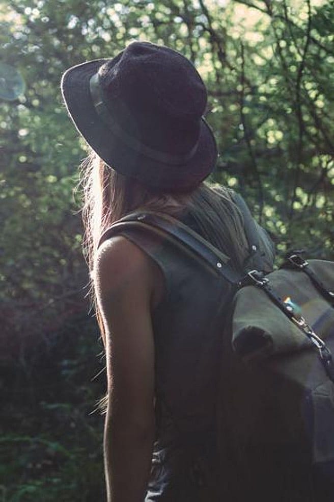 Frau mit Rucksack wandert am Waldrand entlang