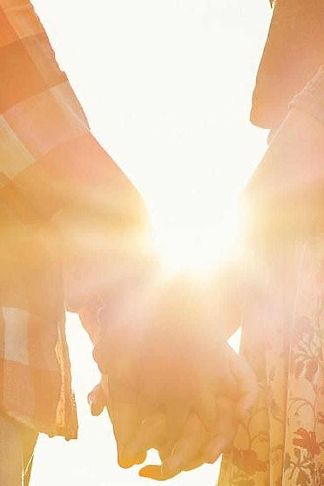 pareja agarrada de la mano en una puesta de sol