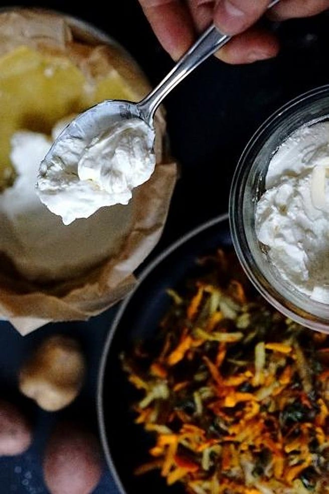 Hand haelt eine Glasschale mit Sauerrahm und einen Loeffel, darunter vorbereitete Kuchenform