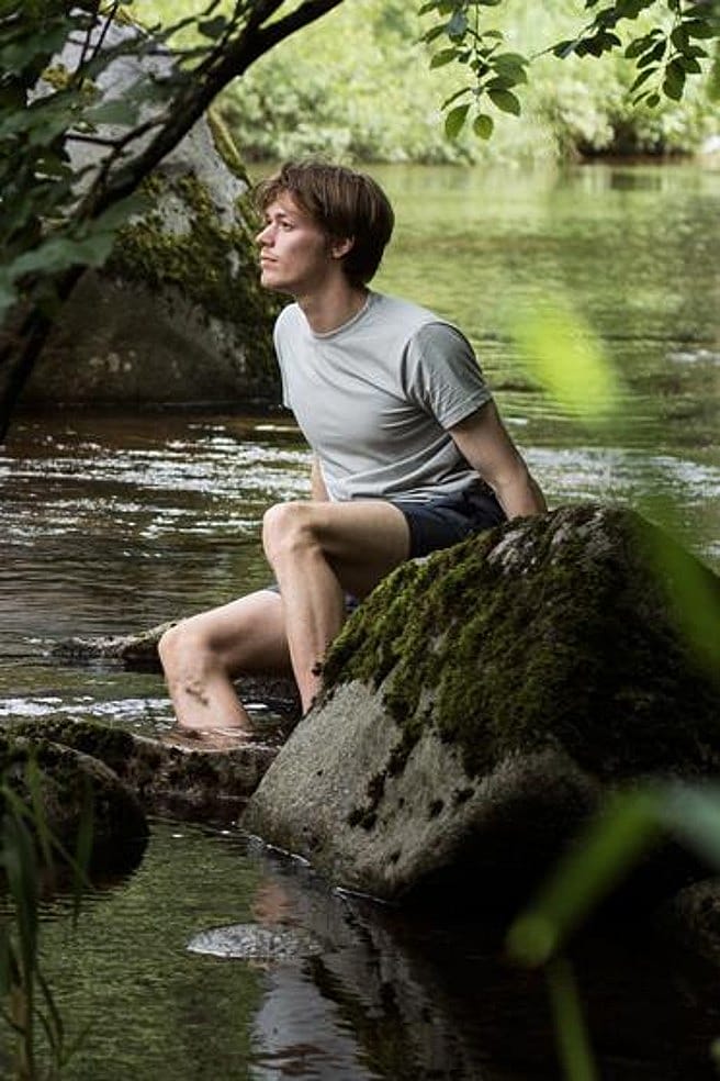 Mann sitzt auf einem Stein im See