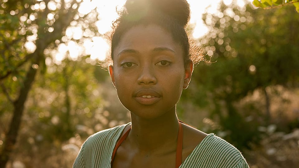 Junge Frau sieht dich an, im Hintergrund die Sonne