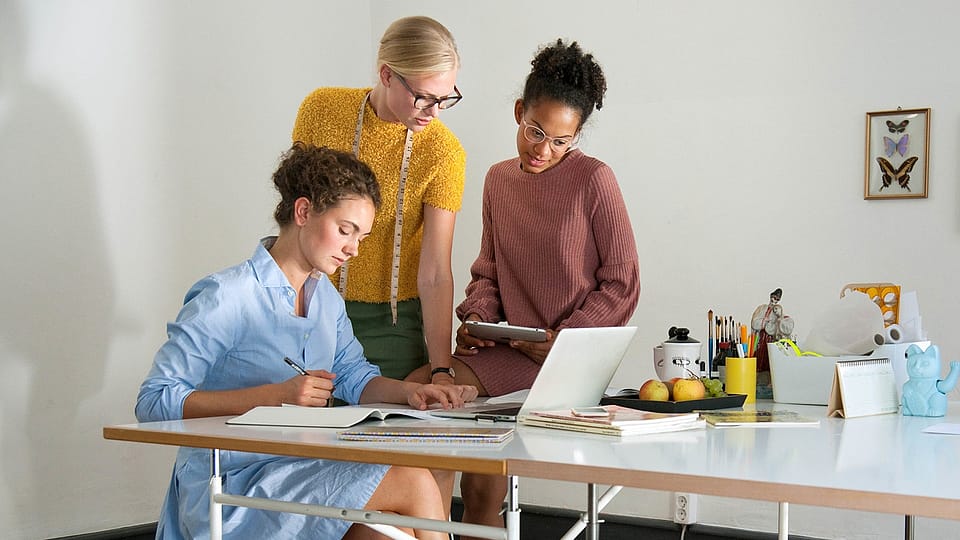 Drei Frauen im Buero am Schreibtisch vor dem Laptop