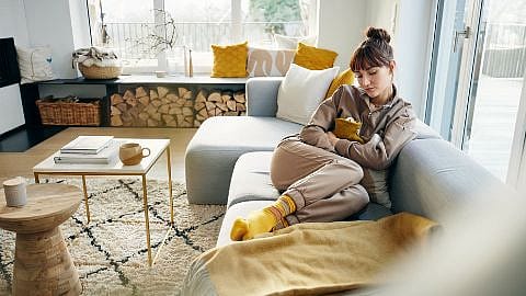 Frau mit Waermflasche auf dem Bauch auf einem Sofa
