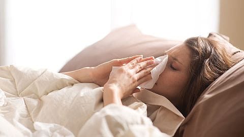 Frau im Bett schneuzt sich die Nase