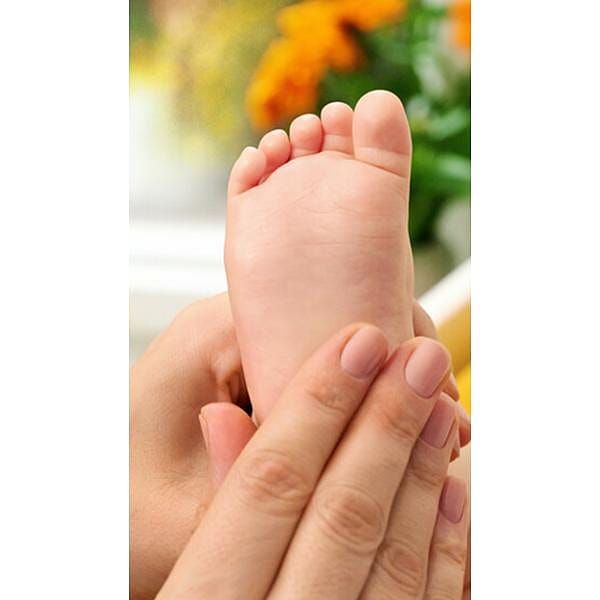 Baby foot being held by adult female hand to prepare for baby massage.