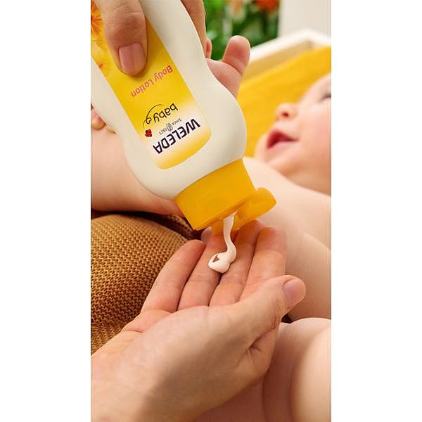 Baby body lotion being poured onto hand before applying to baby on background.