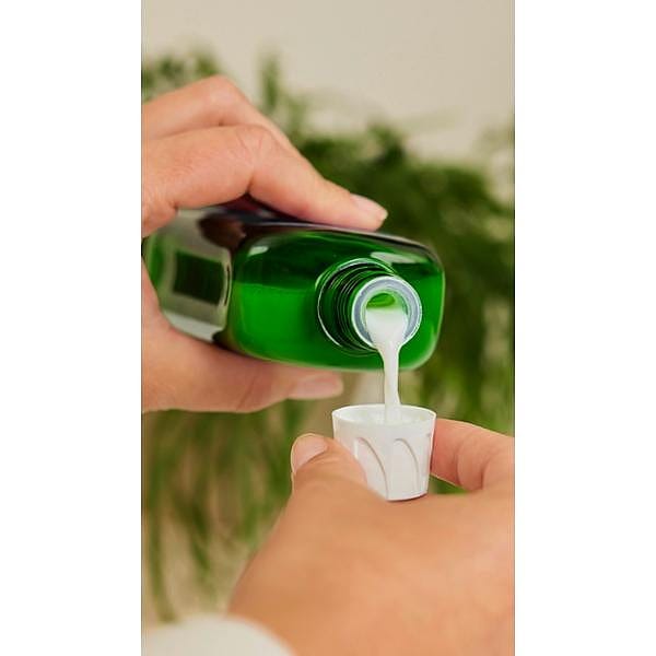 Weleda bath milk pouring from green bottle into bottle cap.