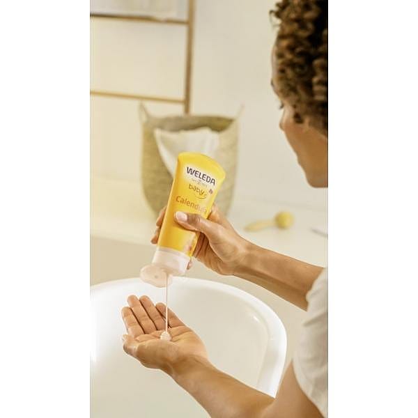 Dark skin mother squeezing Calendula Shampoo & Body Wash onto her hand before adding to baby bath.