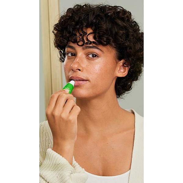 Dark Skin woman holding a Skin Food Lip Balm and applying it to her lips.
