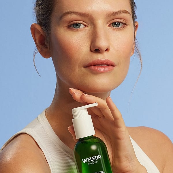 Young woman holdng a bottle of Make-up Removal Cleansing Oil on a light blue background.