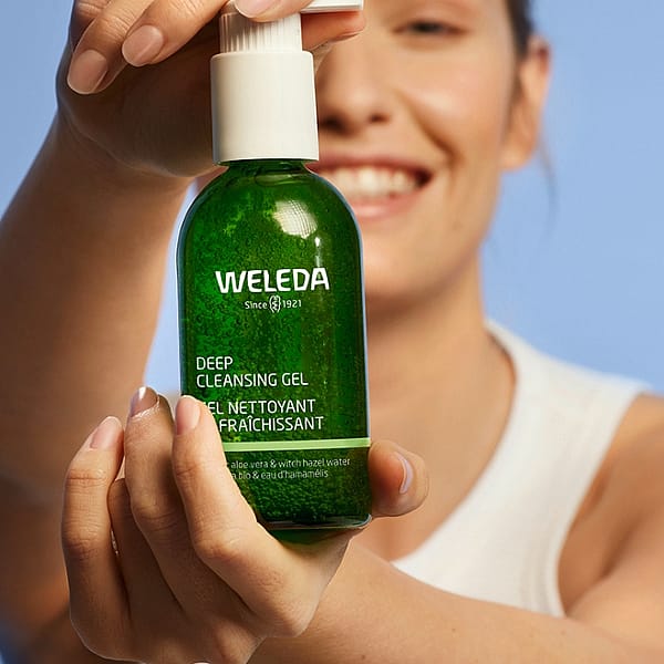 Smiling young woman holding a Deep Cleansing Gel bottle infront of her.