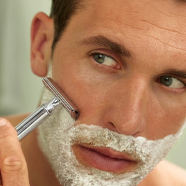 Man looking in the mirrow with shaving cream on his face and holding a razor to his face.