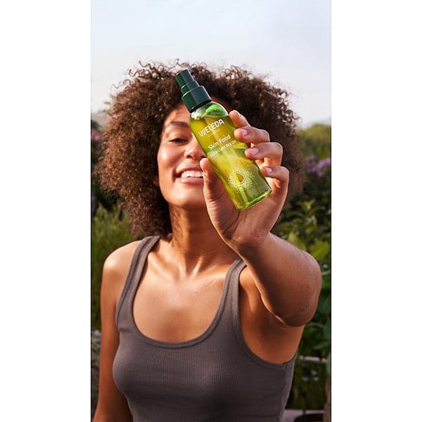 Dark Skin woman holding Skin Food Ultra-Light Dry Oil infront of her.