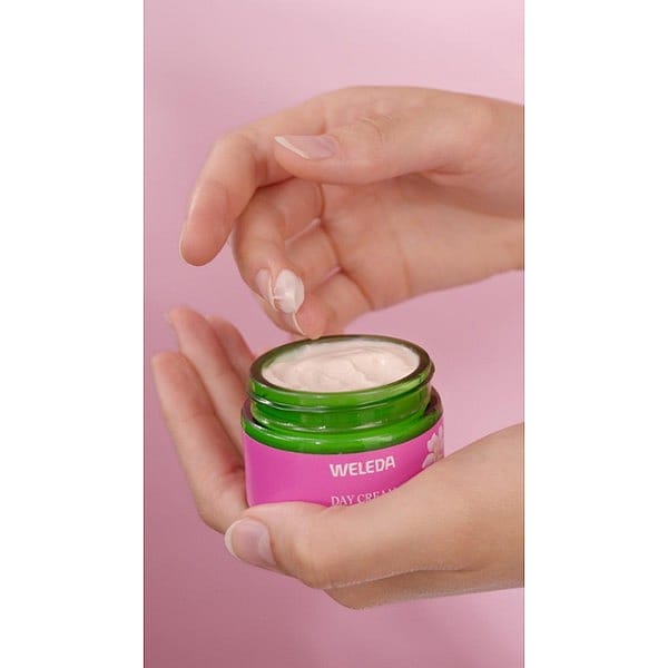 Woman's hand holding an open jar of Smoothing Day Cream Wild Rose & White Tea and dipping a finger into the jar.