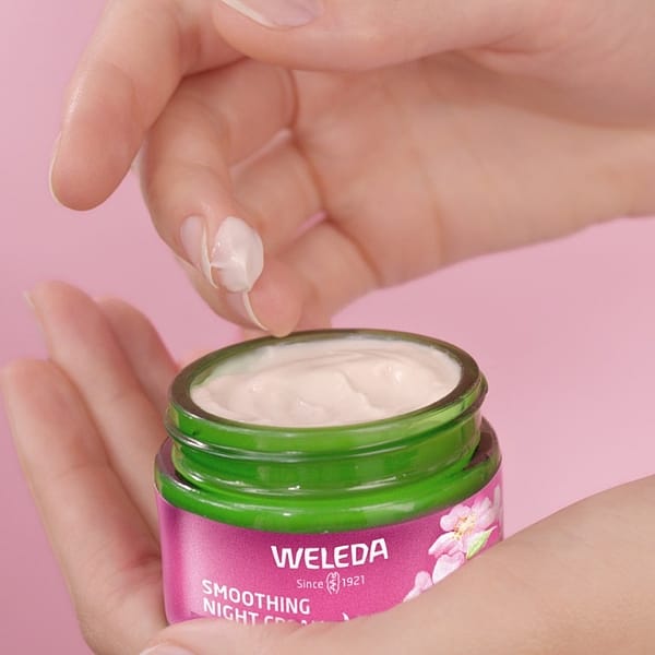 Woman's hand holding an open jar of Smoothing Night Cream Wild Rose & White Tea and dipping a finger into the jar.