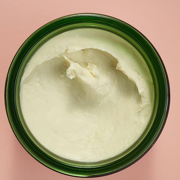 Open Stretch Mark Body Butter jar showing texture on a pink background.