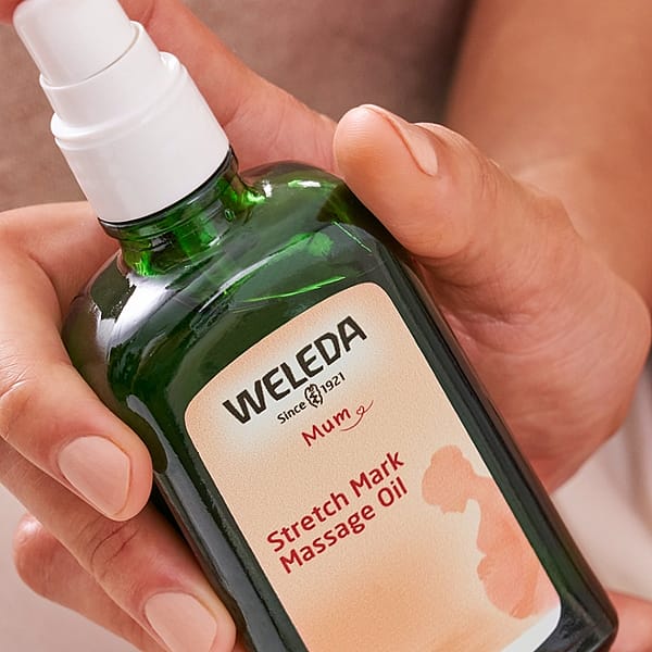 Stretch Mark Massage Oil bottle held by a woman's hand.