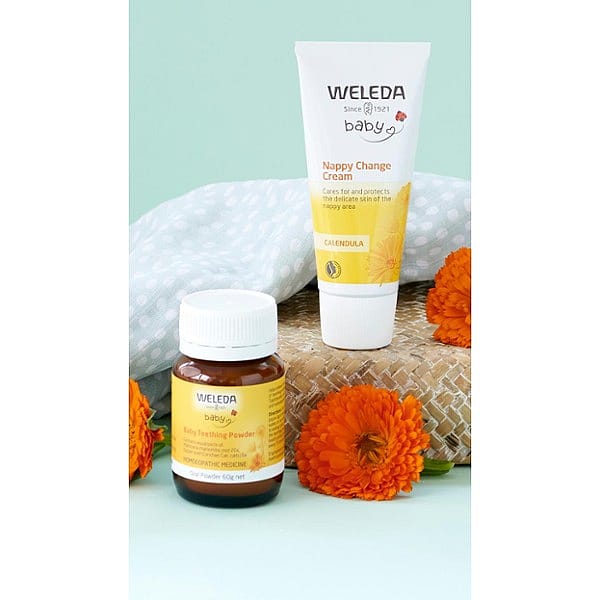 Calendula Nappy Change Cream and Baby Teething Powder next to orangle flowers.